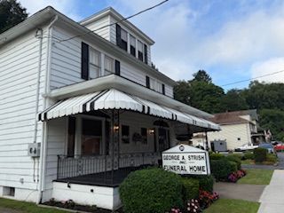 White two-story building with a black and white striped awning; George A. Strish Funeral Home sign.