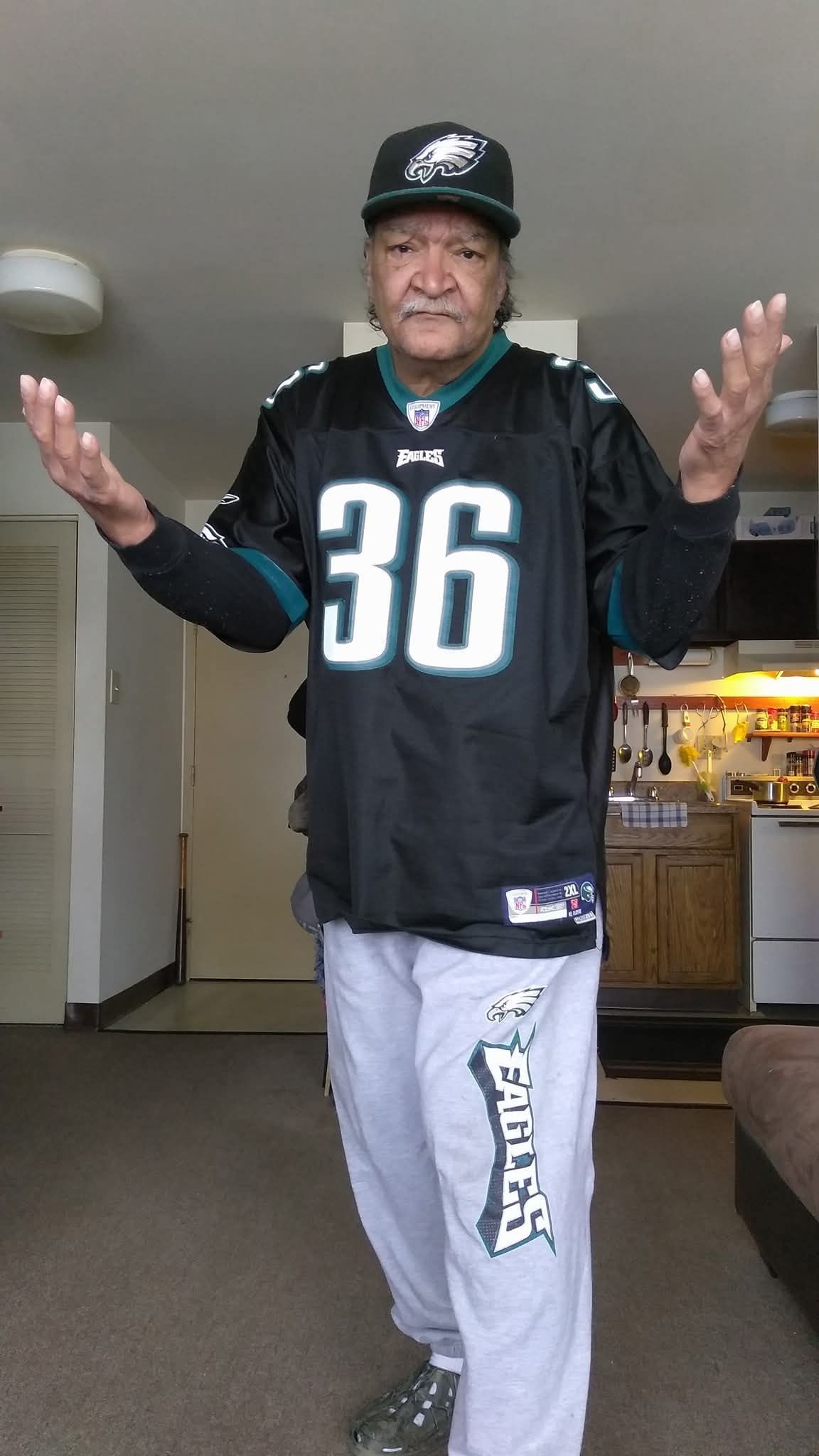 Man wearing a black sports jersey and cap, standing indoors with arms raised