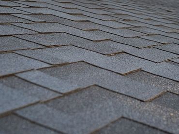 Close-up of gray asphalt roof shingles with overlapping rows and slight weathering