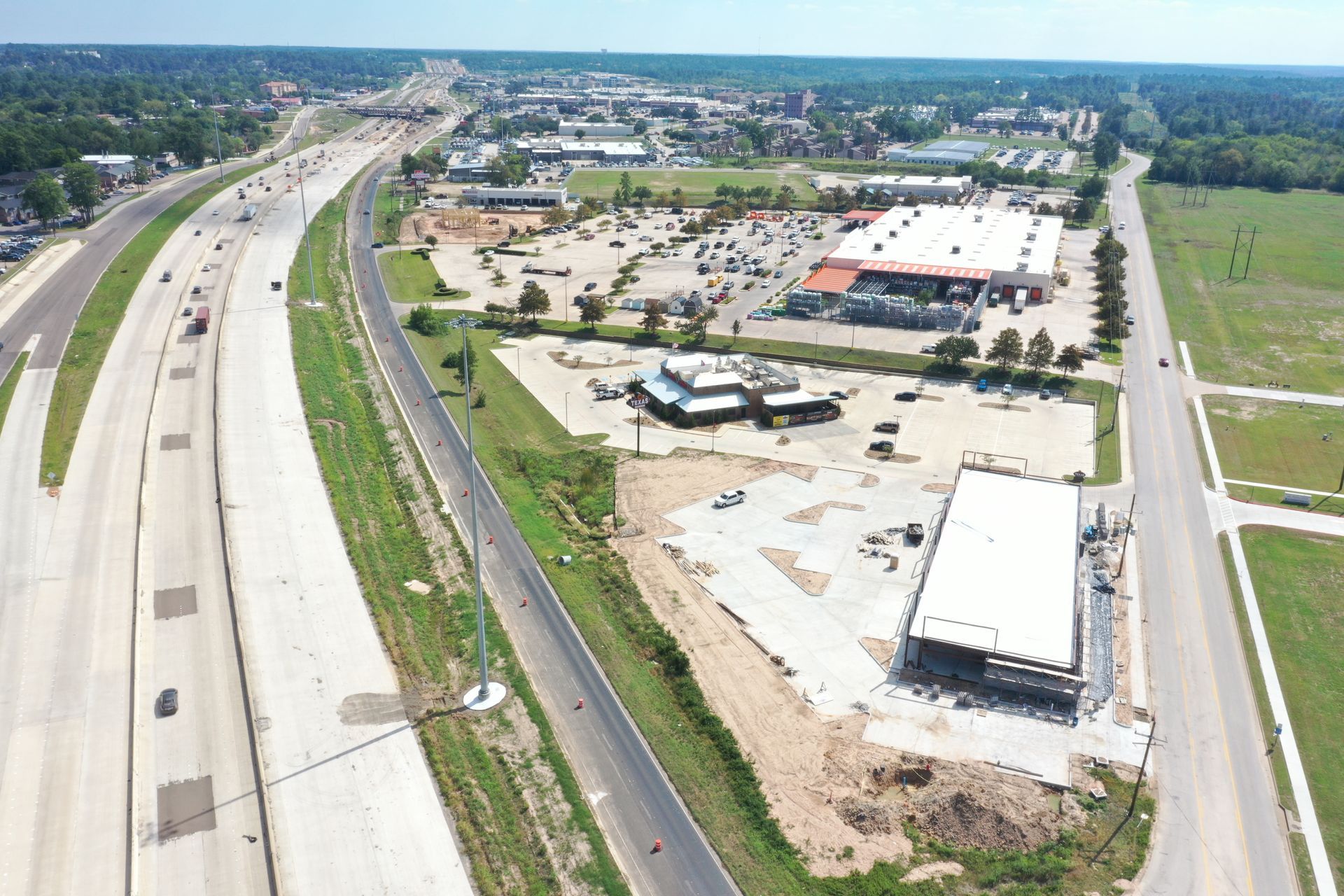 Aerial view of a highway and roadside commercial lot with buildings, parking areas, and open land