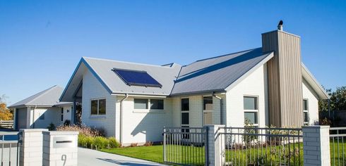Modern white house with solar panels and a fenced yard under a clear sky