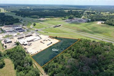 Aerial view of a construction site beside a green airfield and wooded area, with one plot marked “Site”