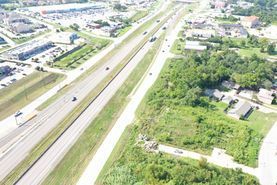 Aerial view of a highway with light traffic beside green fields and nearby buildings
