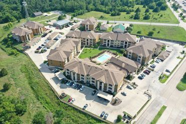Aerial view of a large apartment complex with parking lots, trees, and a swimming pool