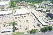 Aerial view of a large shopping center with parking lots, cars, and surrounding buildings.