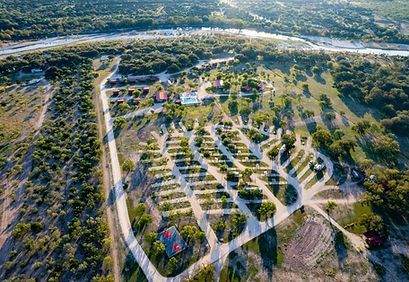 Aerial view of a winding road through a rural campground with many white-roofed cabins and scattered trees