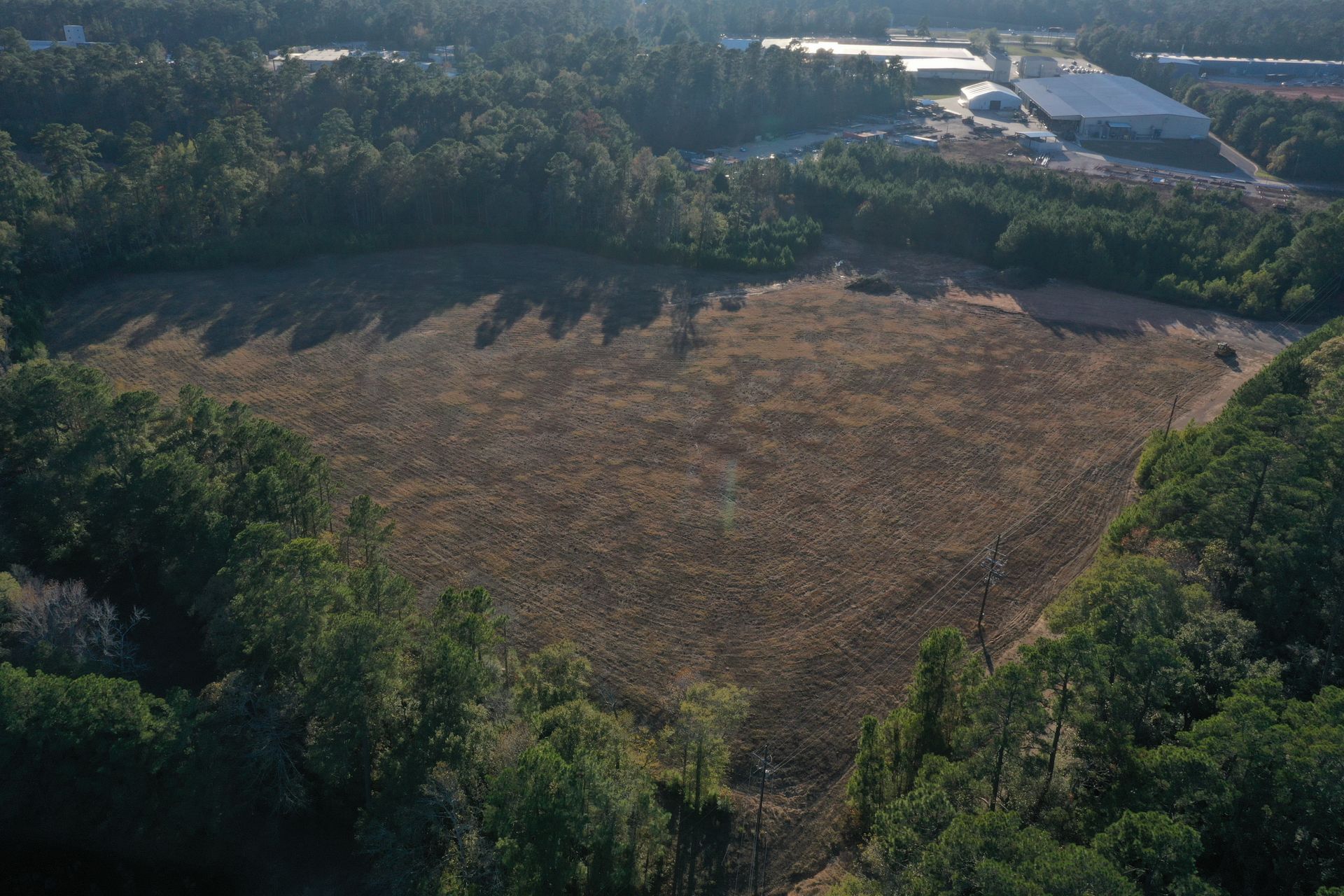 Aerial view of a large cleared field surrounded by dense green trees and a road in the distance