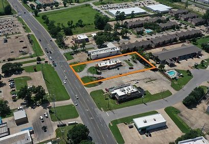 Aerial view of a neighborhood with an orange-outlined lot and buildings beside a busy road.