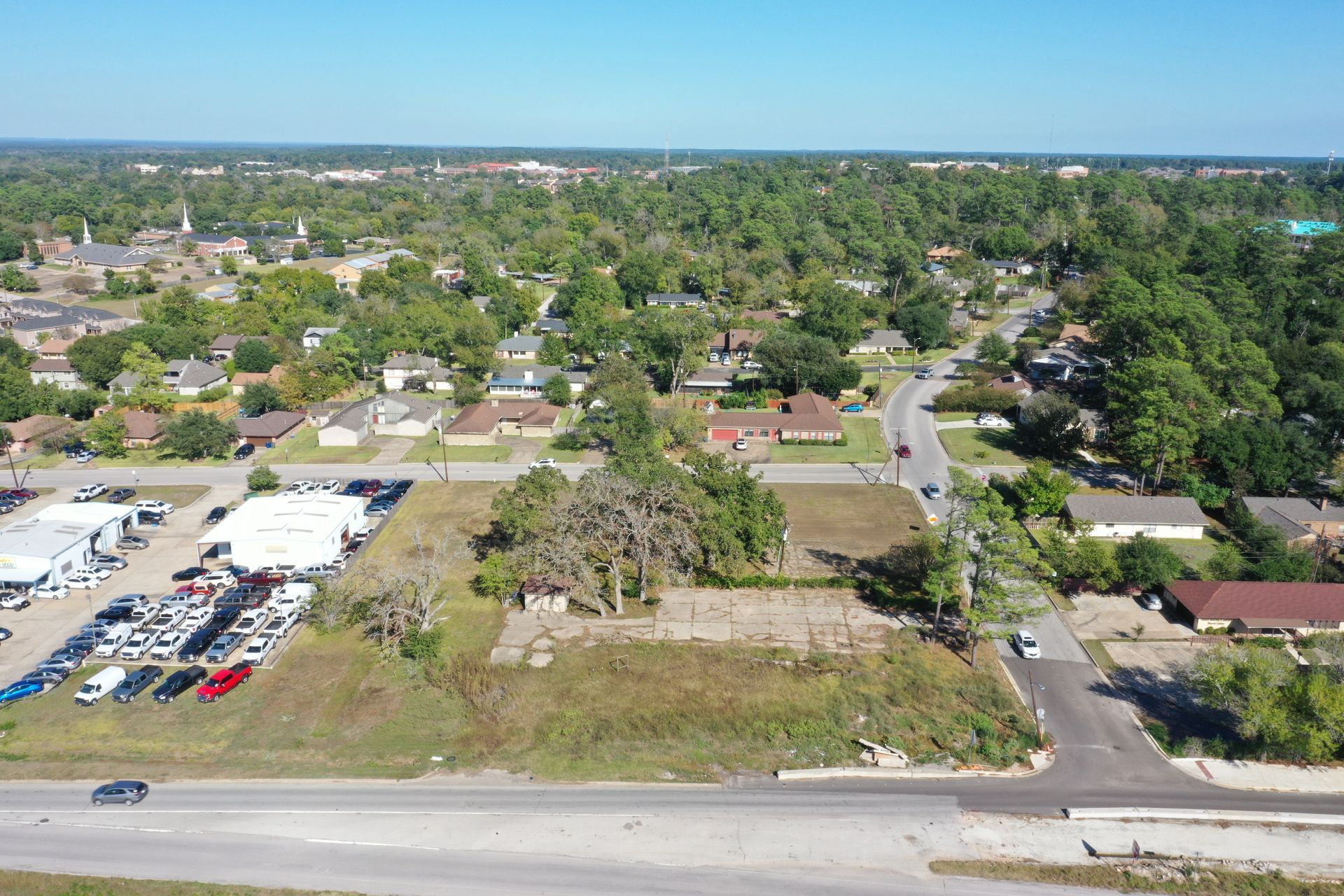 Aerial view of a suburban neighborhood with roads, houses, trees, and a parking lot on a sunny day