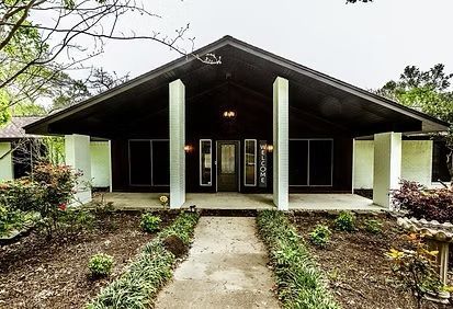 Front view of a modern house with a covered porch, tall columns, and a garden-lined walkway
