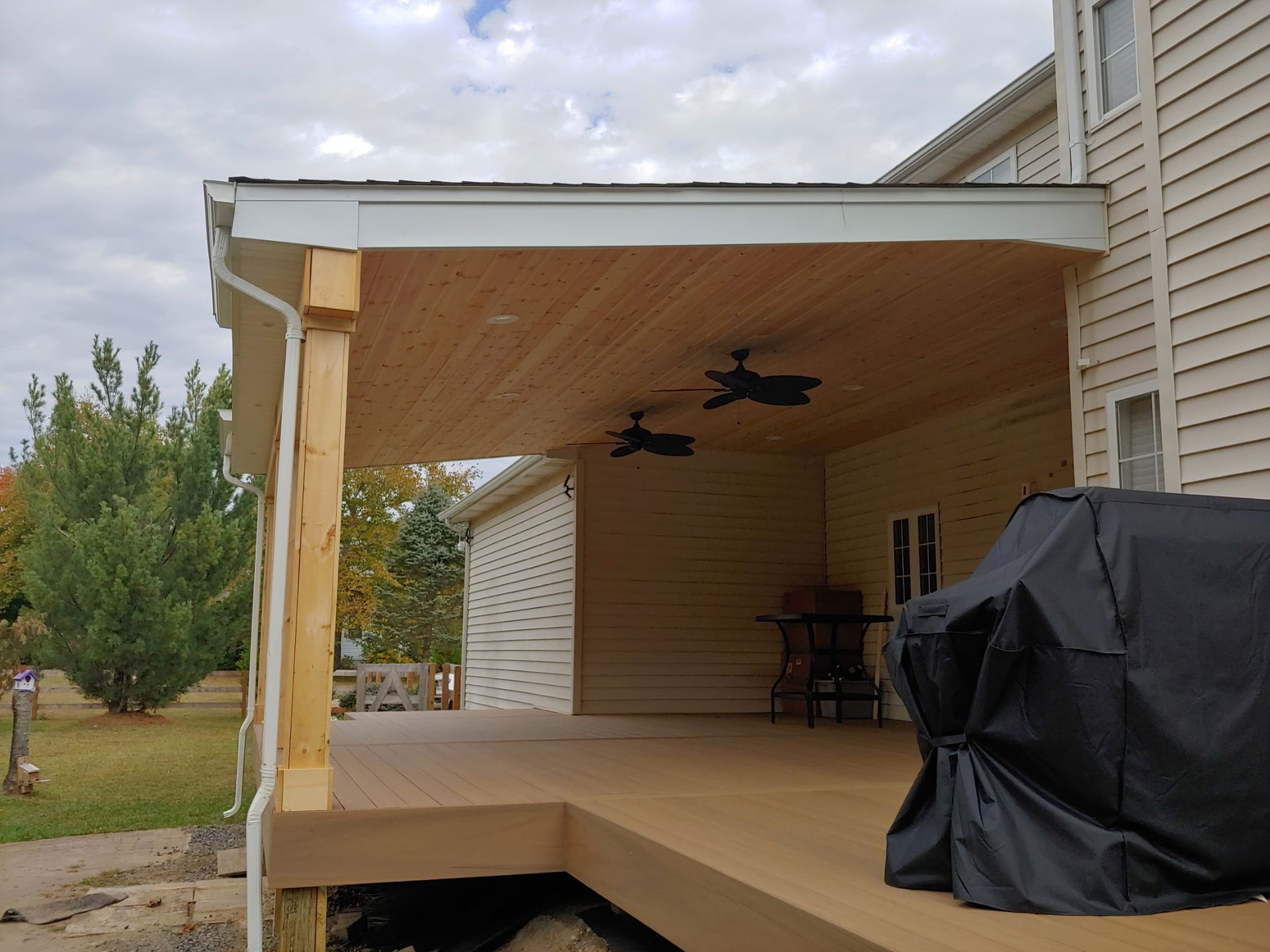 A wooden deck with a ceiling fan and a grill on it.