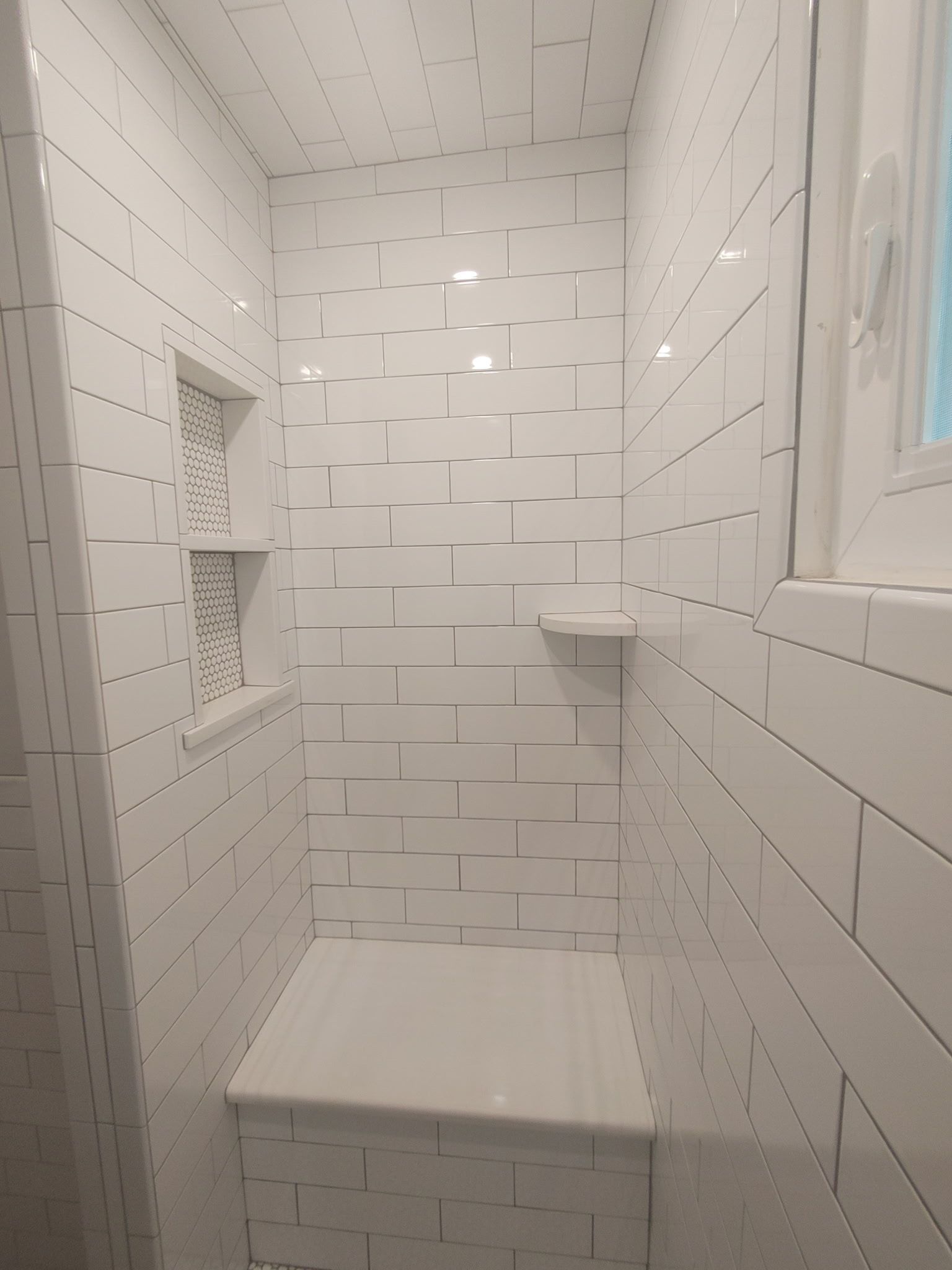 A bathroom with white tiles and a window.