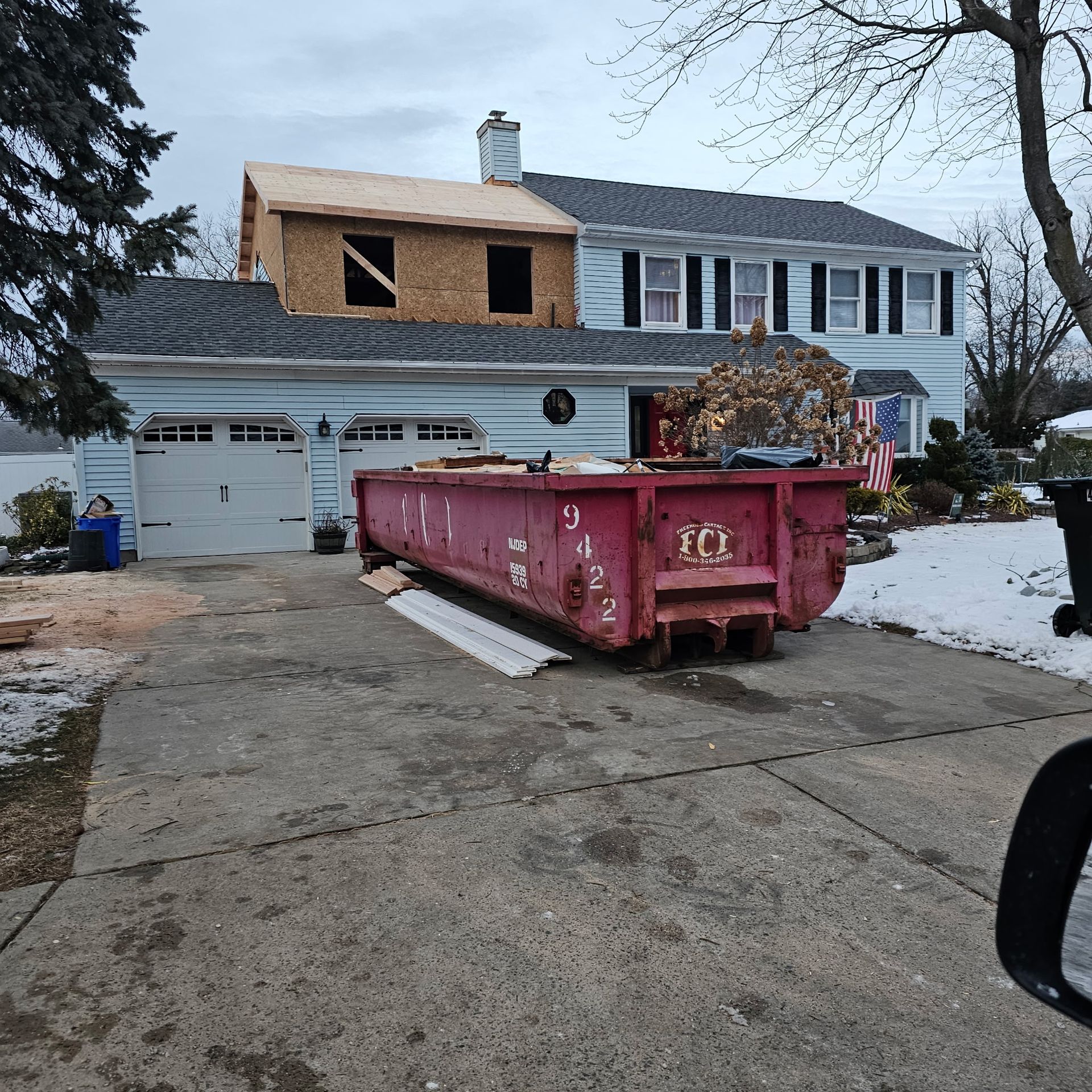 A large red dumpster is parked in front of a house under construction