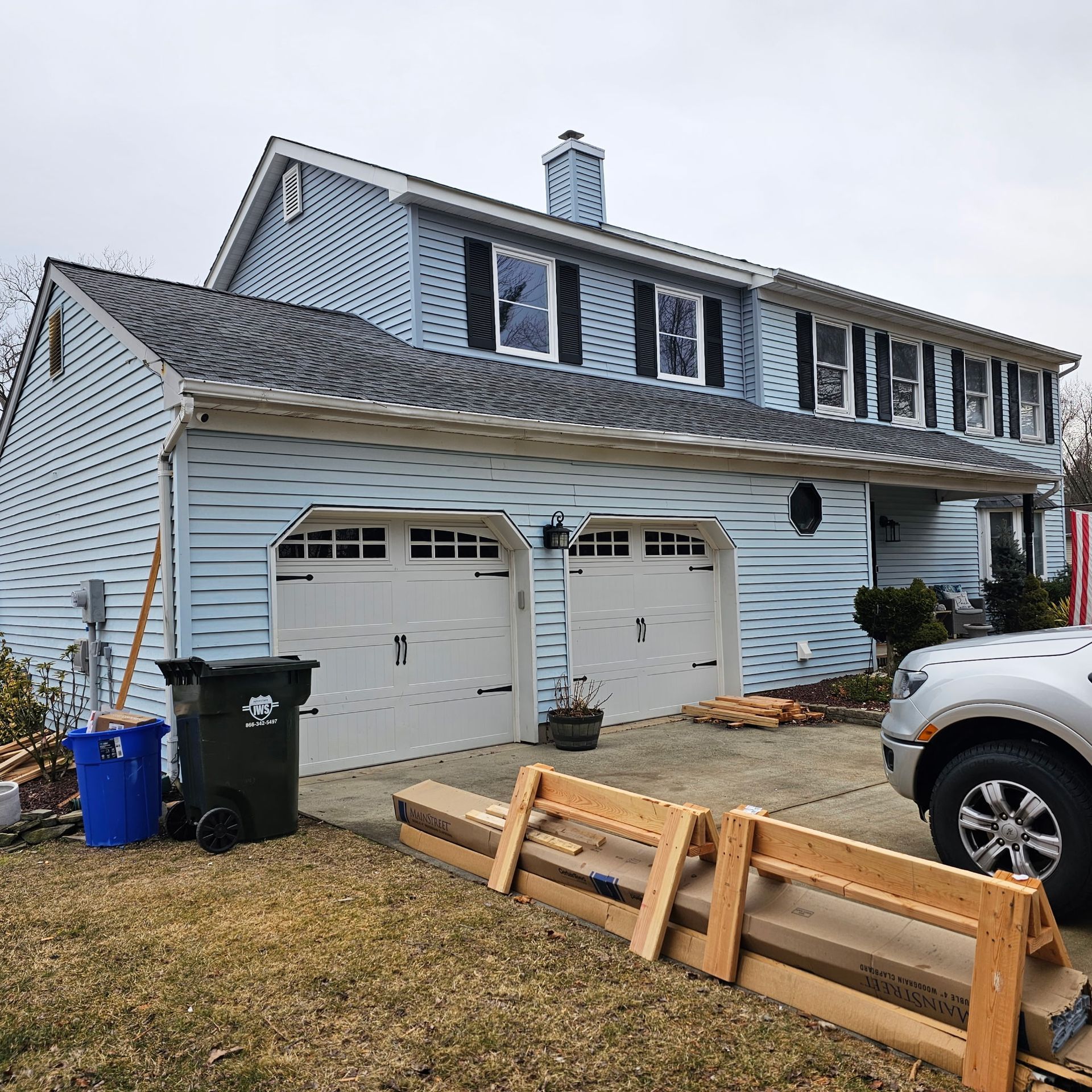 A car is parked in front of a house with two garage doors