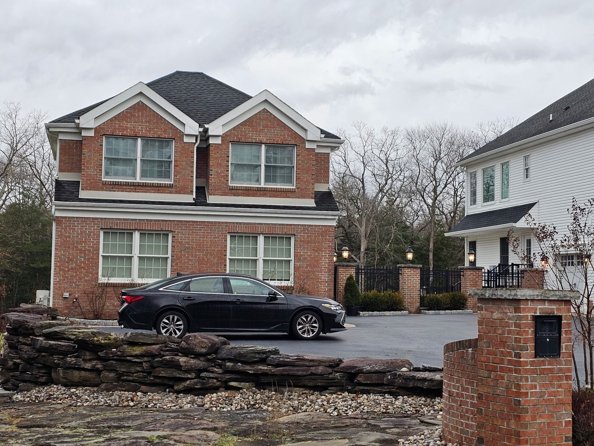 A black car is parked in front of a brick house
