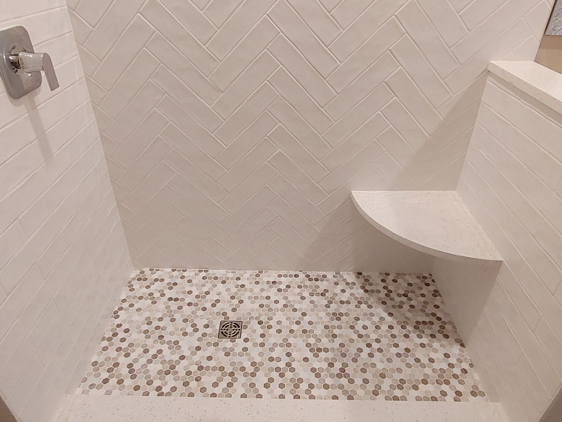 A walk in shower with a bench and white tiles.