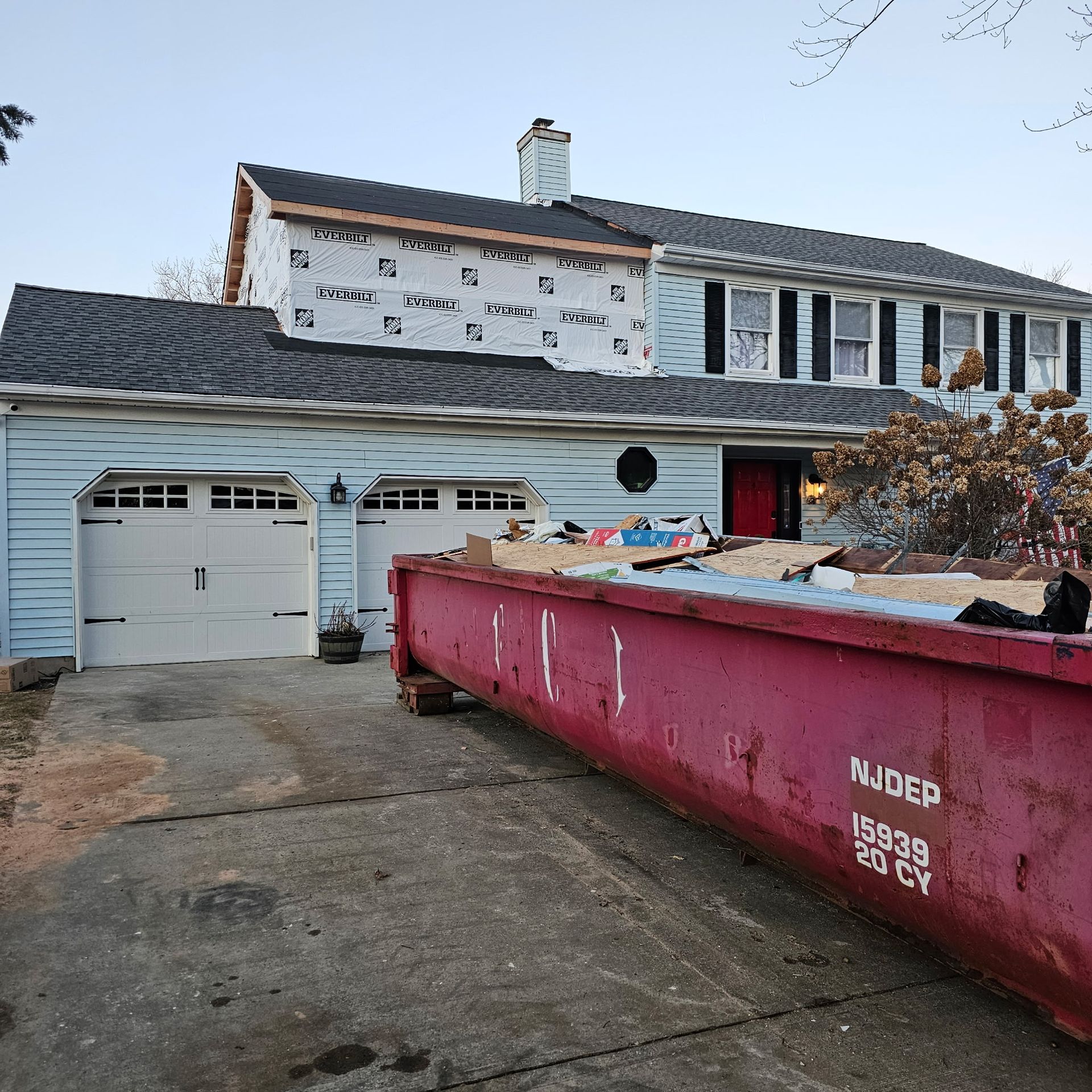 A large red dumpster is parked in front of a house