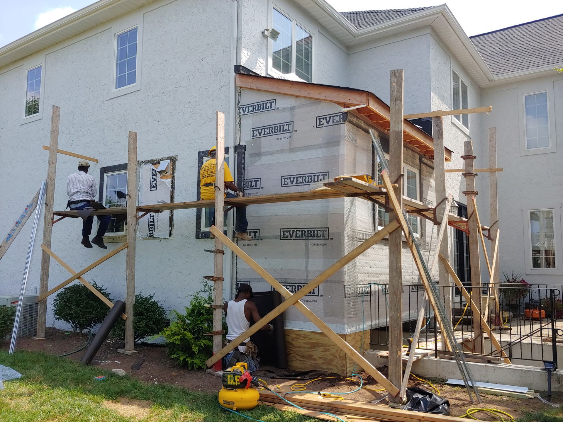 A large white house is being remodeled with wooden scaffolding.