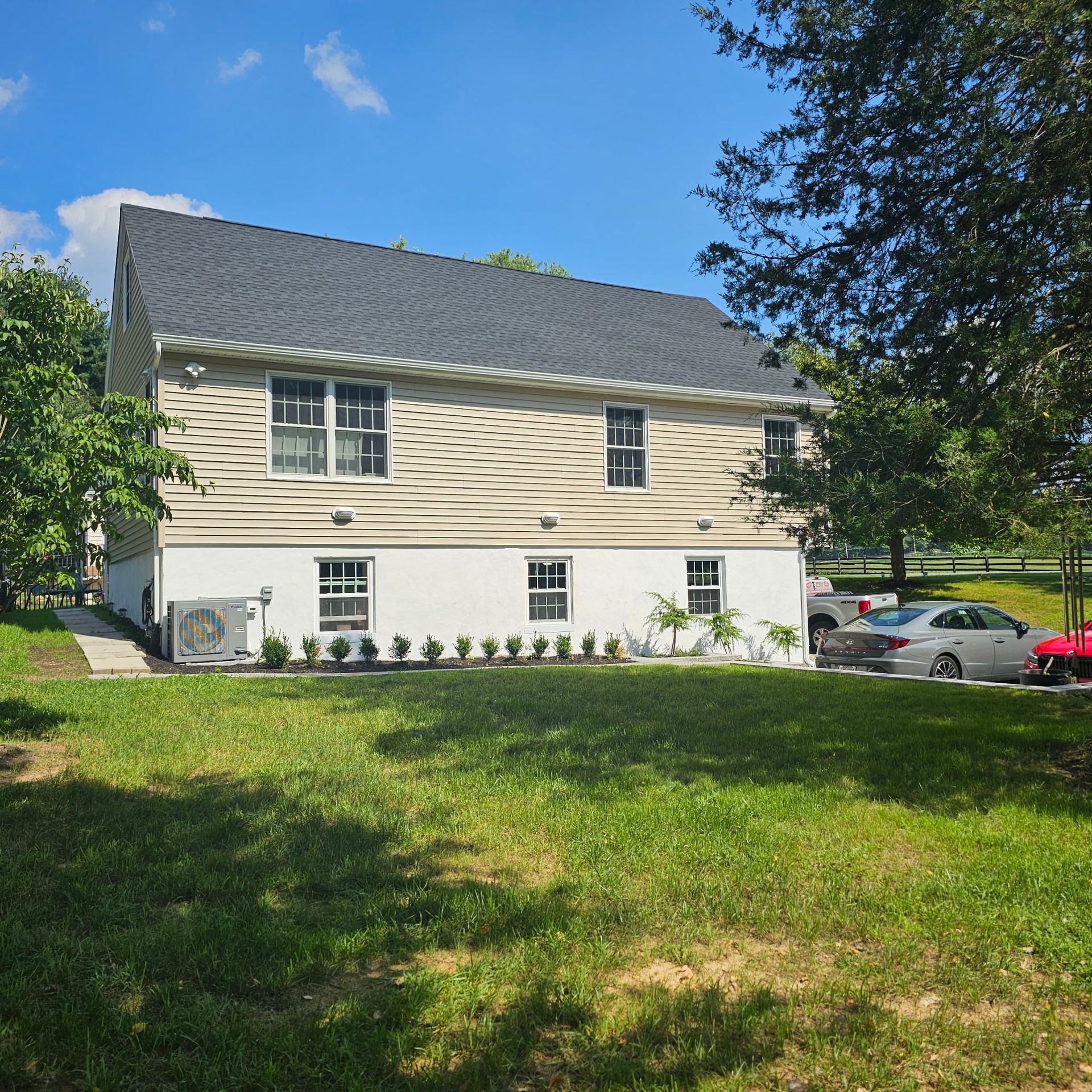 A white house with a gray roof sits in the middle of a lush green field