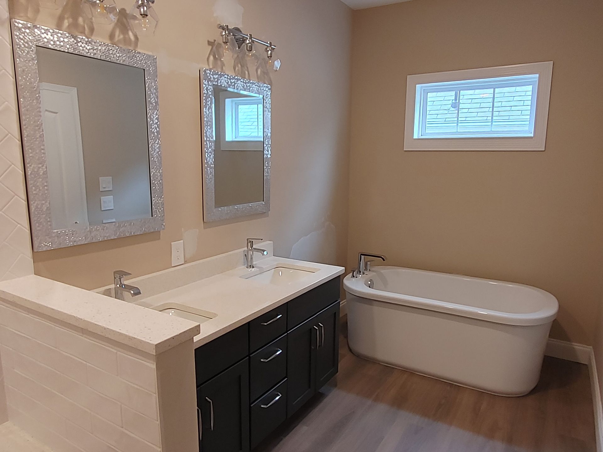 A bathroom with two sinks , a tub , two mirrors and a window.
