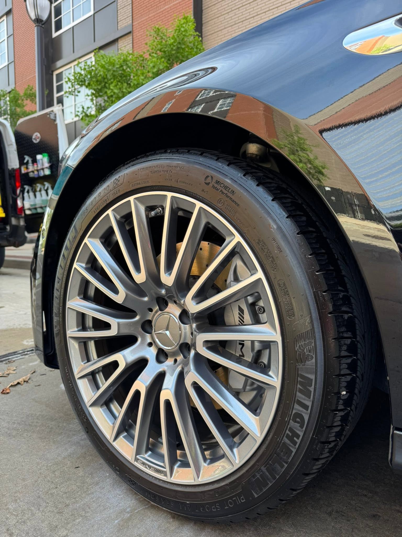 Close-up of a black car’s shiny alloy wheel and tire parked on a city street