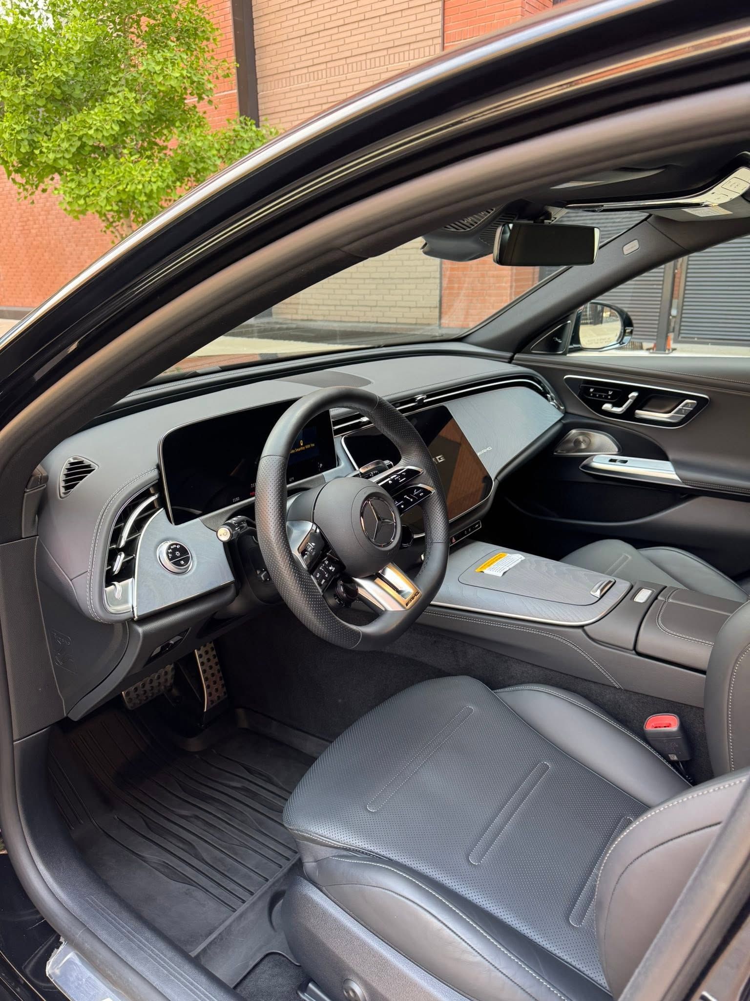 Open car door showing a black leather driver’s seat, steering wheel, dashboard, and center console.