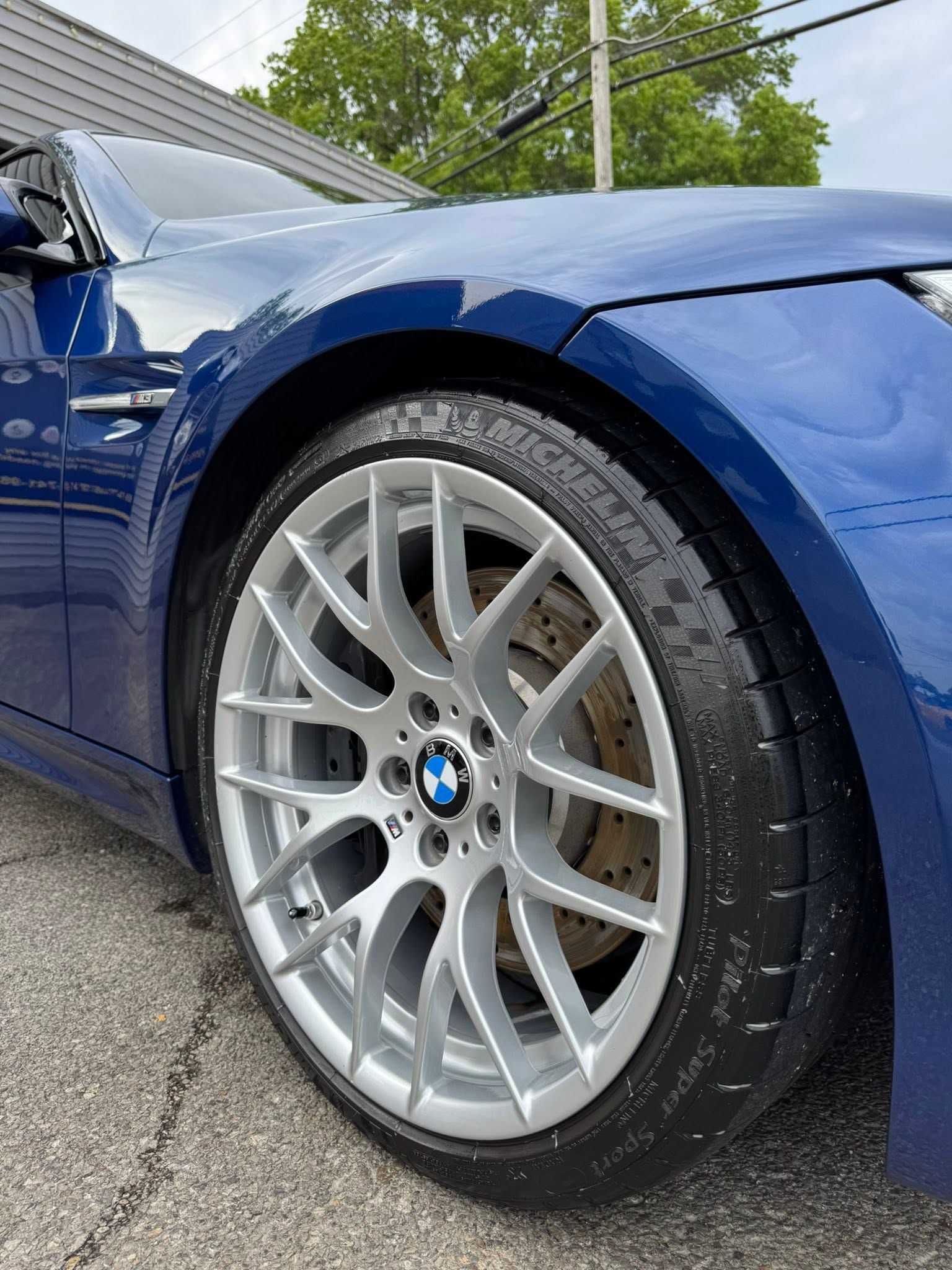 Blue BMW with silver alloy wheel parked outdoors, close-up of front tire and fender