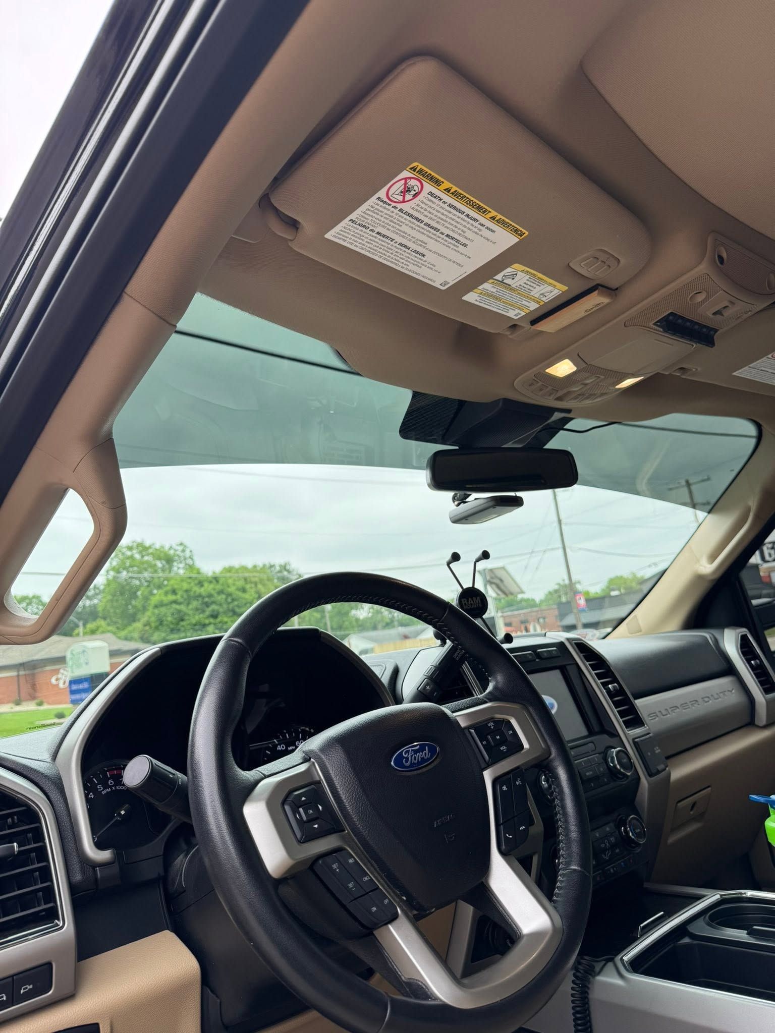 Car interior with steering wheel, dashboard, sunroof, and road view through the windshield.