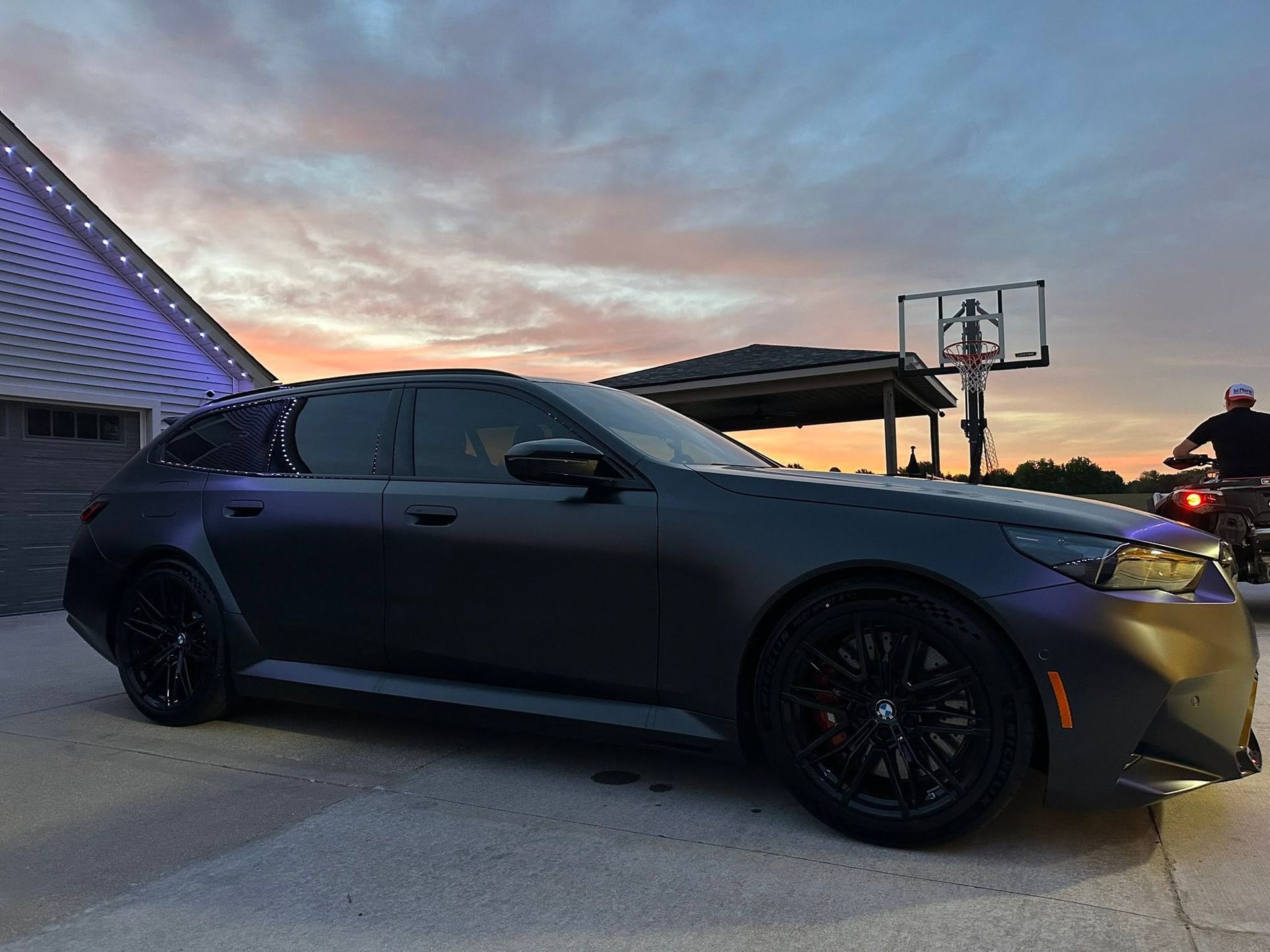Matte black sports sedan parked outdoors at dusk beside a modern building.