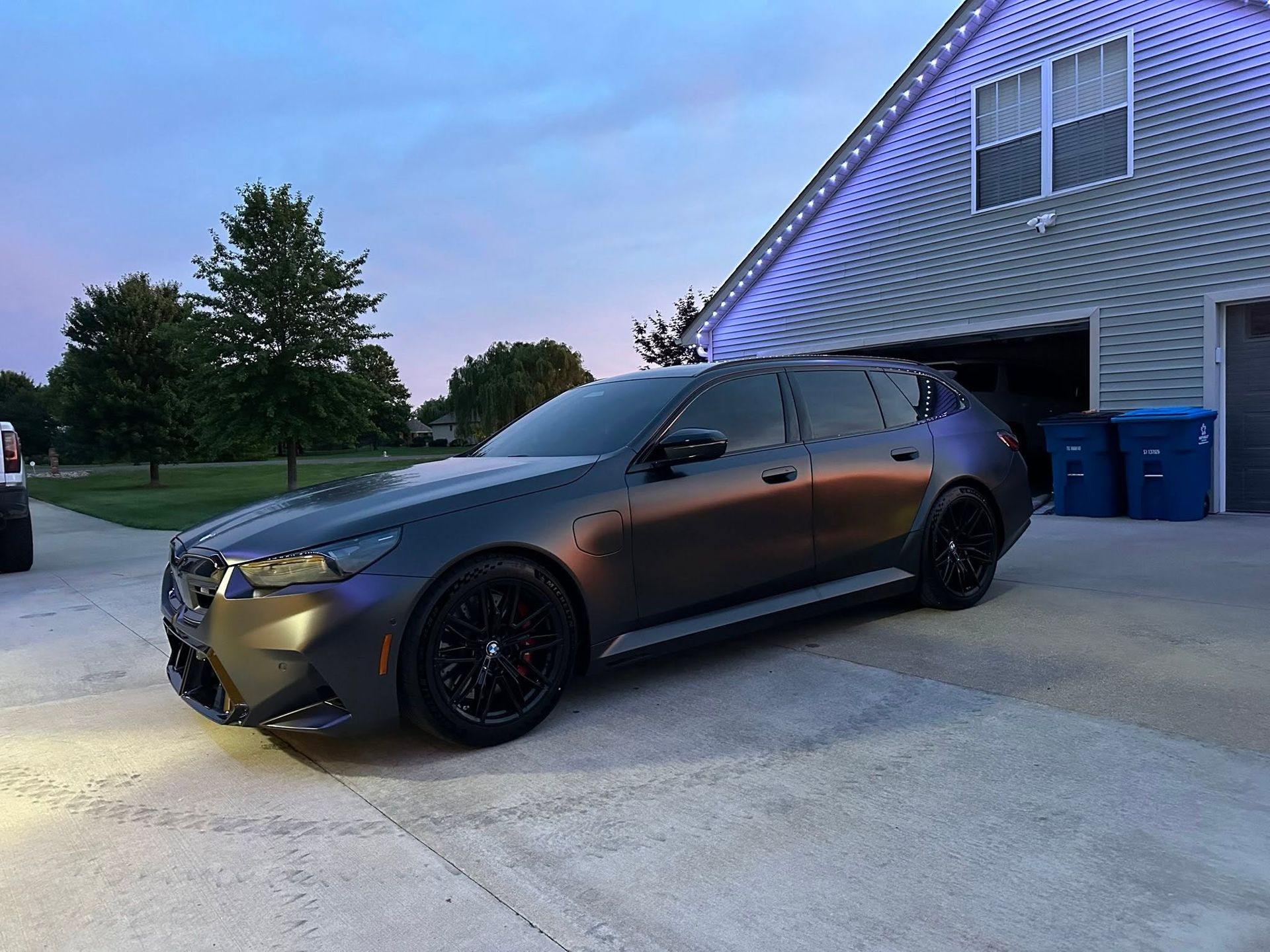 Dark gray sports sedan parked in a driveway beside a house at dusk