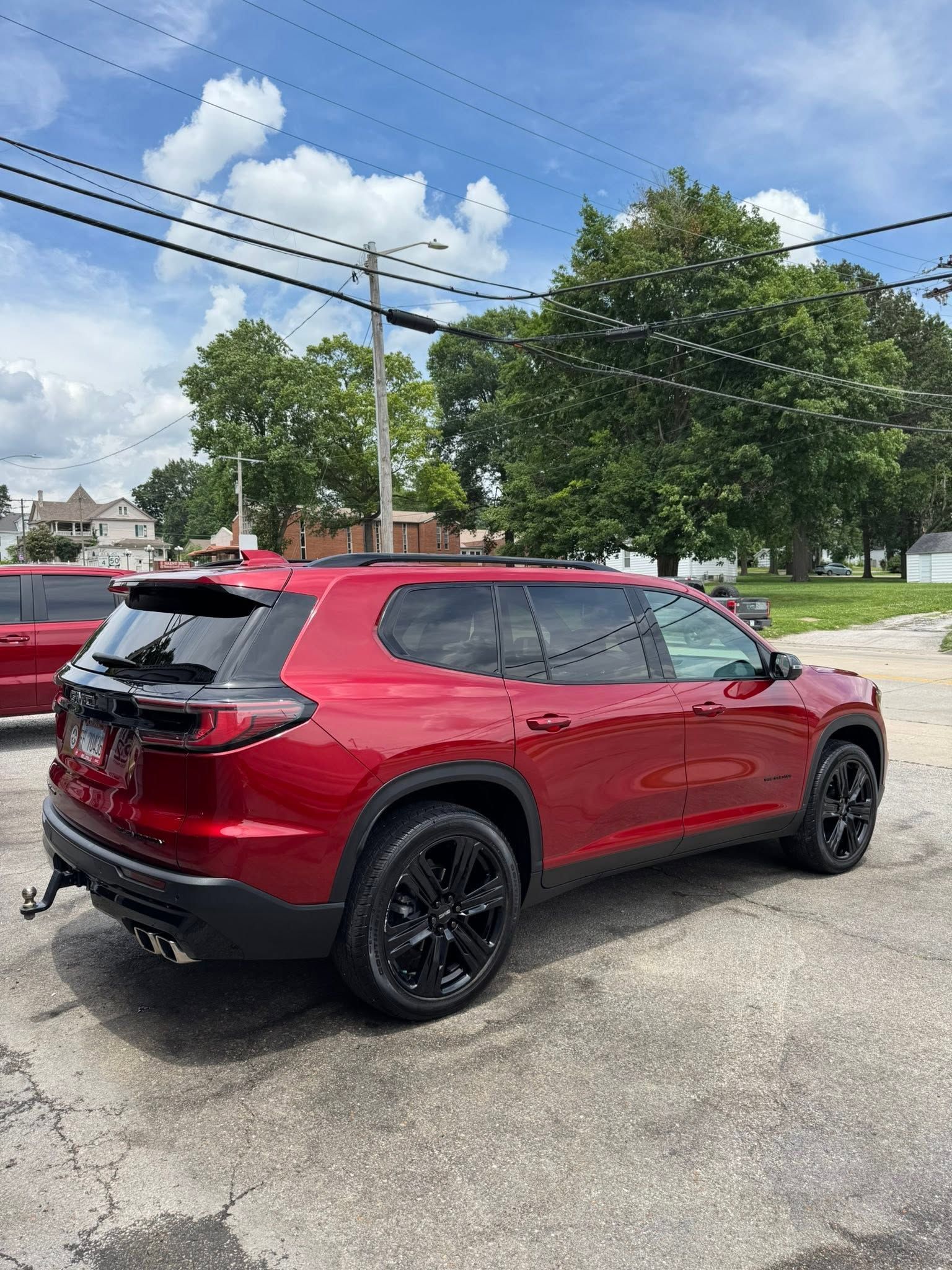 Red SUV parked on a lot under a partly cloudy sky, with trees and power lines in the background.