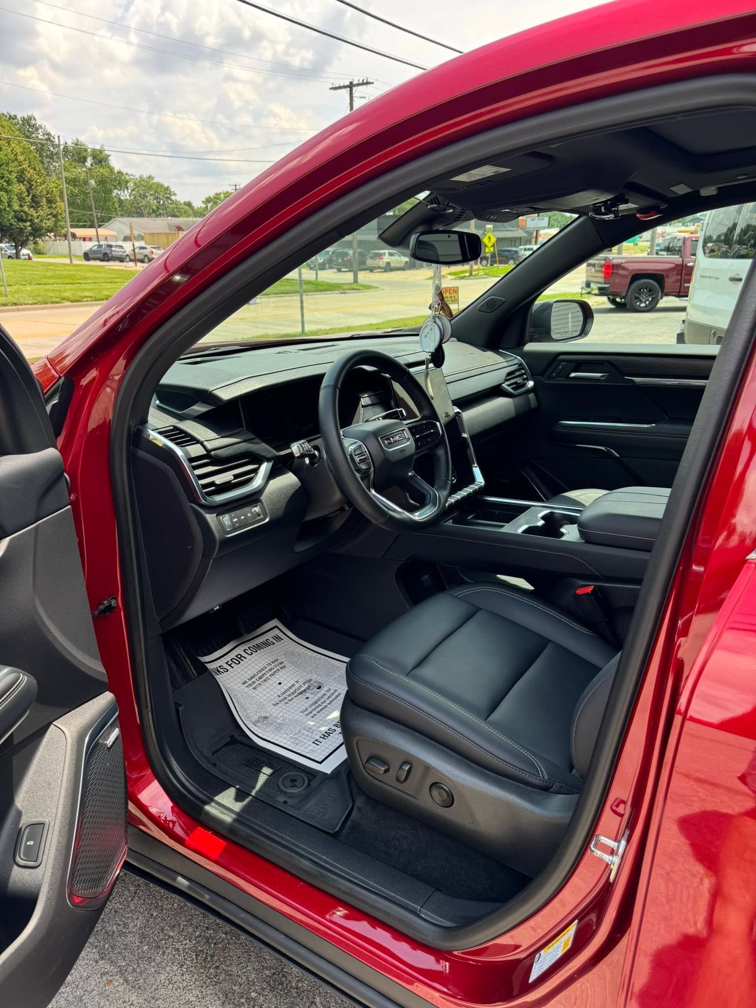 Open driver’s door of a red car, showing black leather interior and dashboard.
