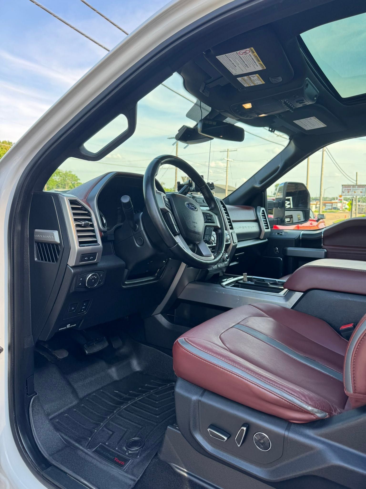 Luxury truck interior with burgundy leather seats, steering wheel, and open driver’s door.