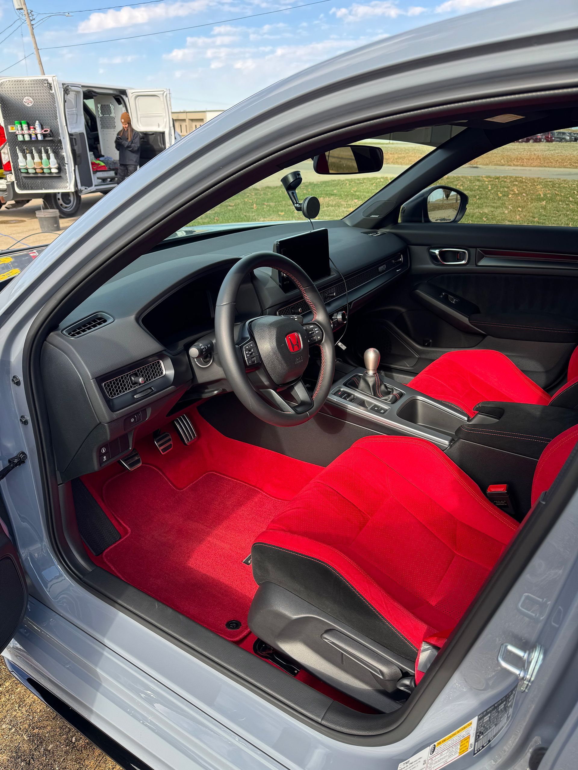 Sports car interior with red seats and carpet, black dashboard, and open door at an outdoor event