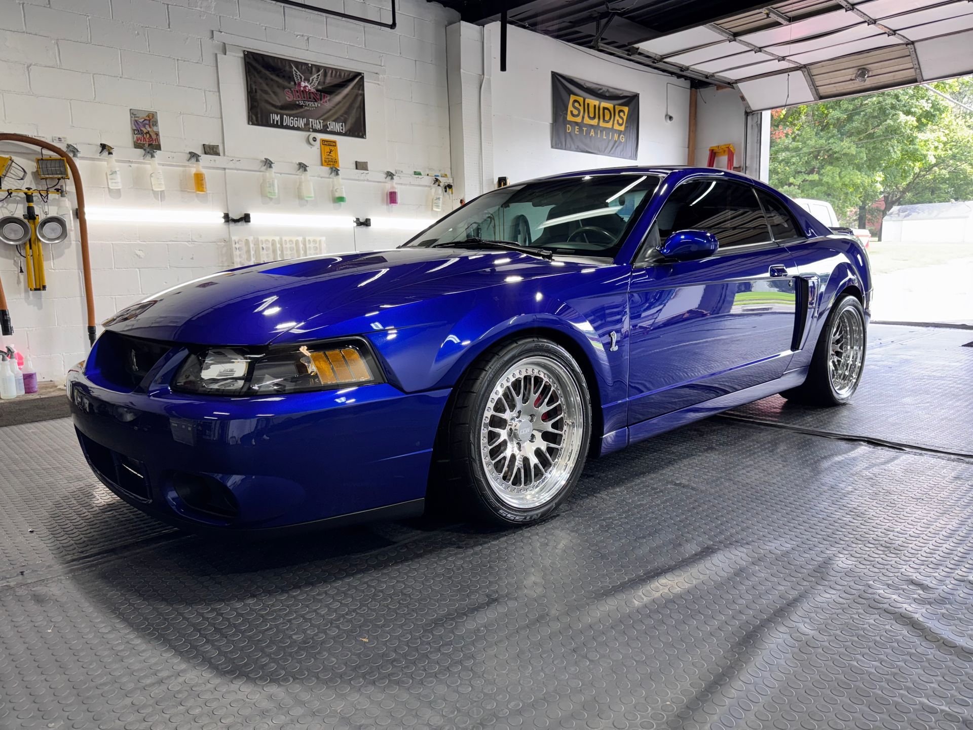 Blue sports coupe parked indoors on a garage floor, front-left angle.