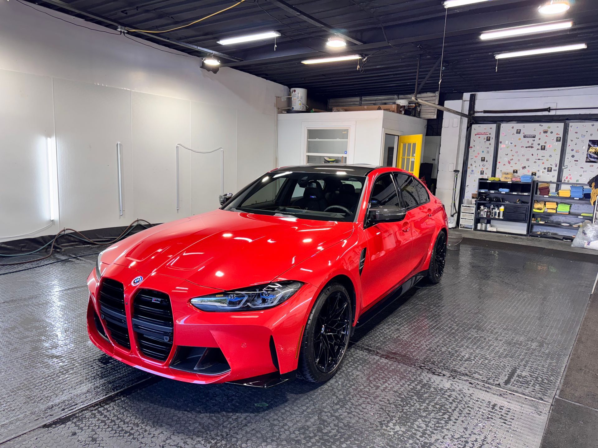 Red sports sedan in a detailing garage, bright red paint with black grille and wheels.