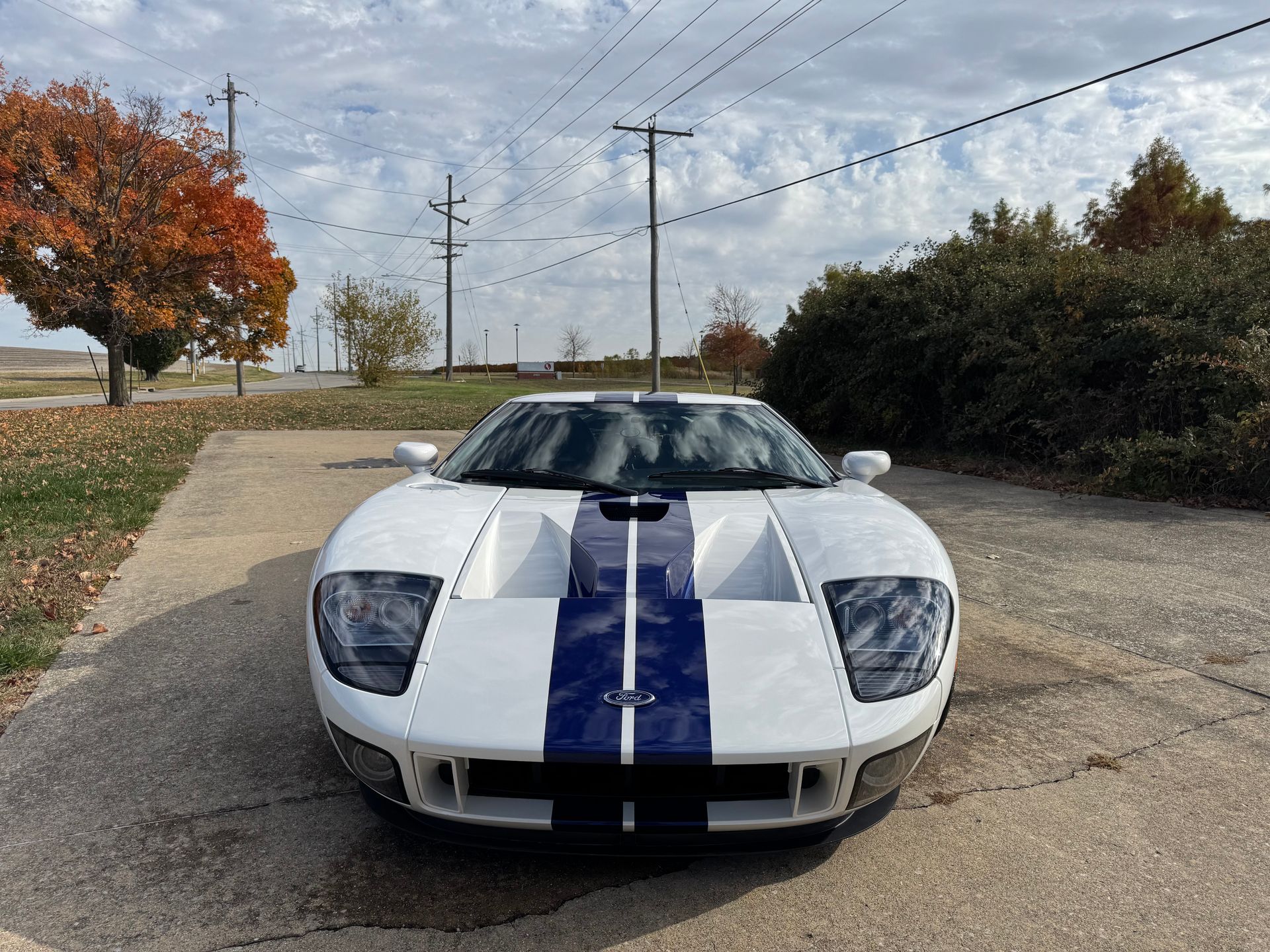 White sports car with blue racing stripes parked on a gravel road under a cloudy sky