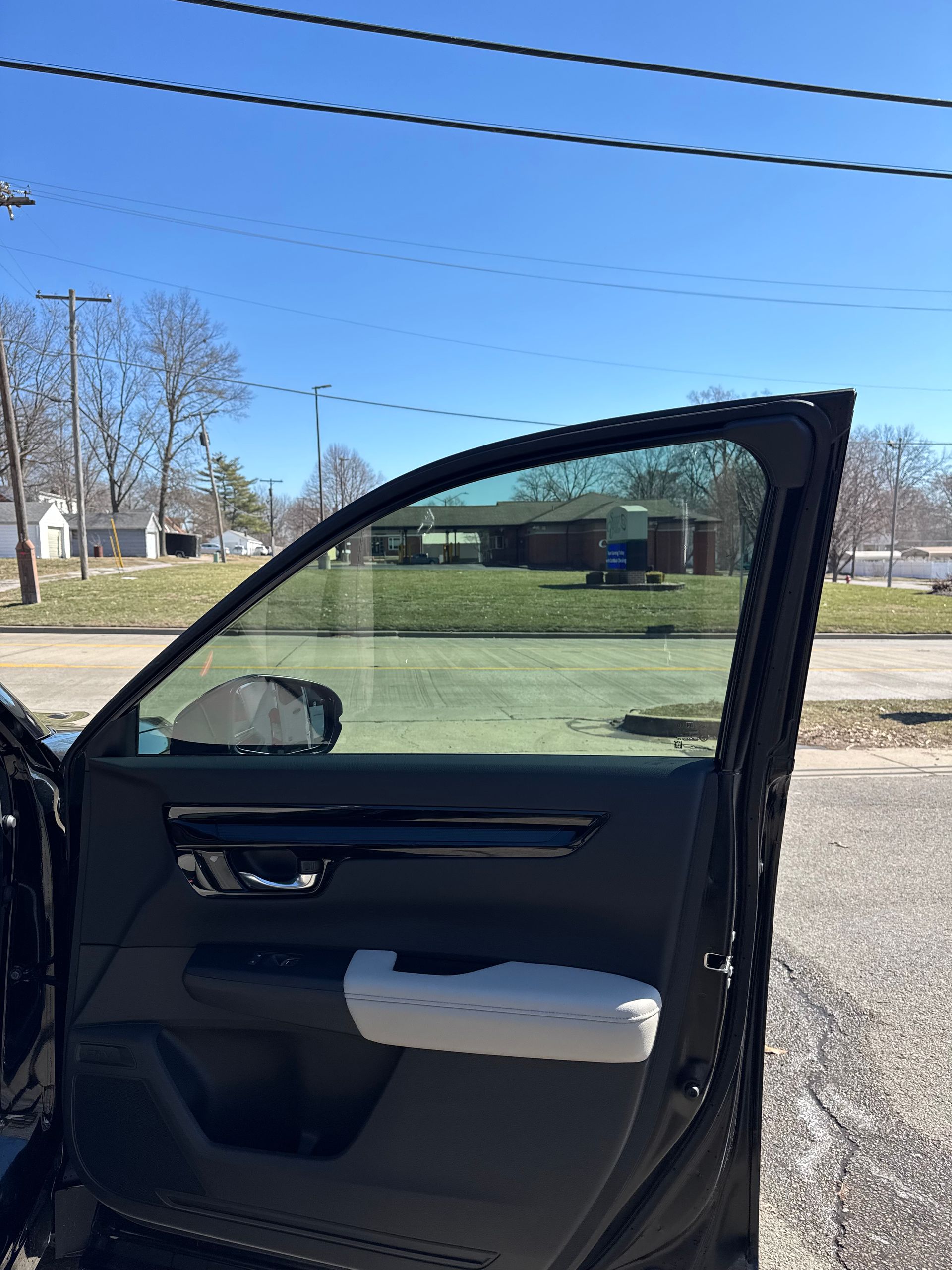 Open car door with tinted window in a sunny outdoor parking area