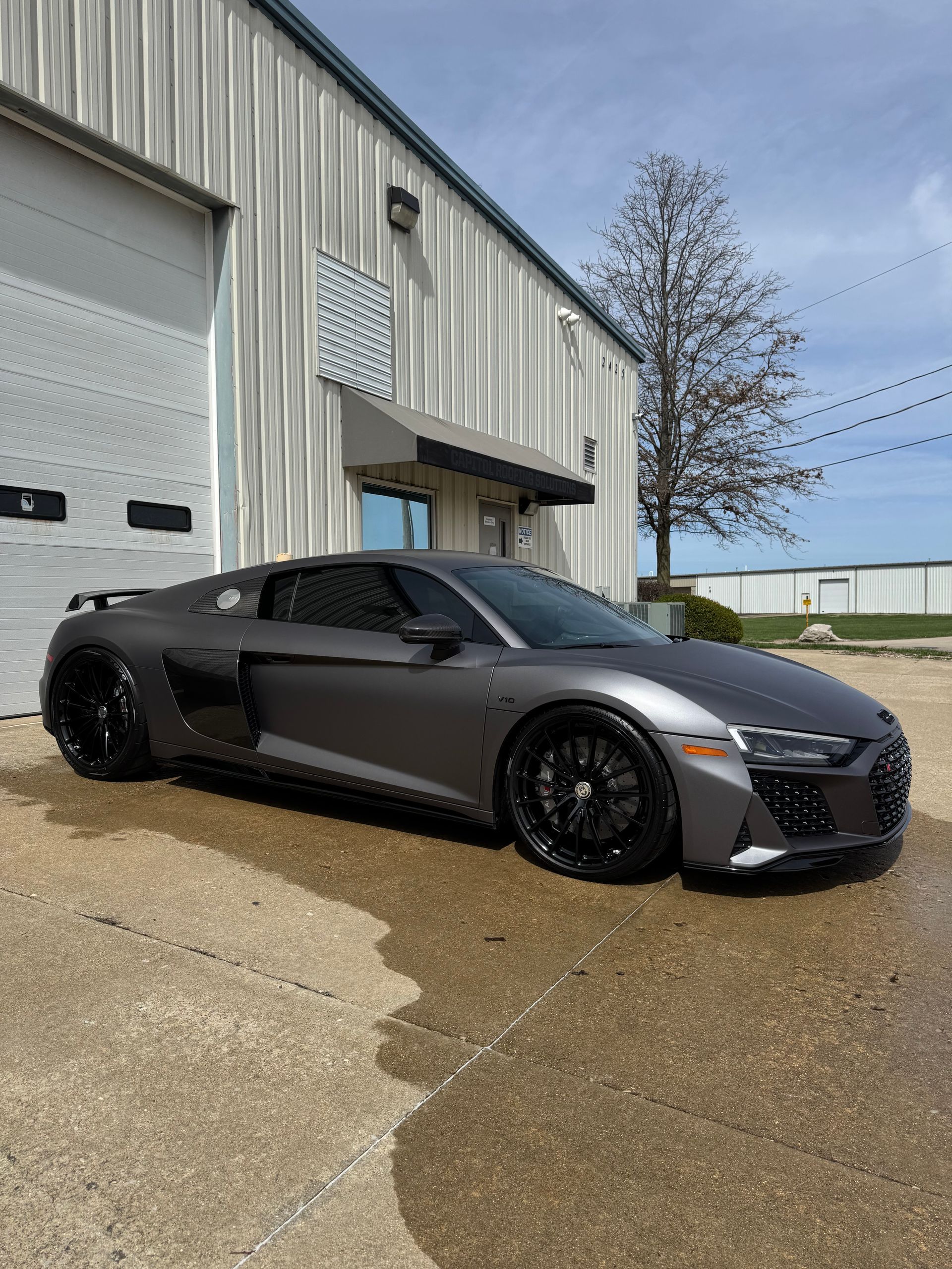 Dark gray sports car parked outside a metal warehouse on a wet lot