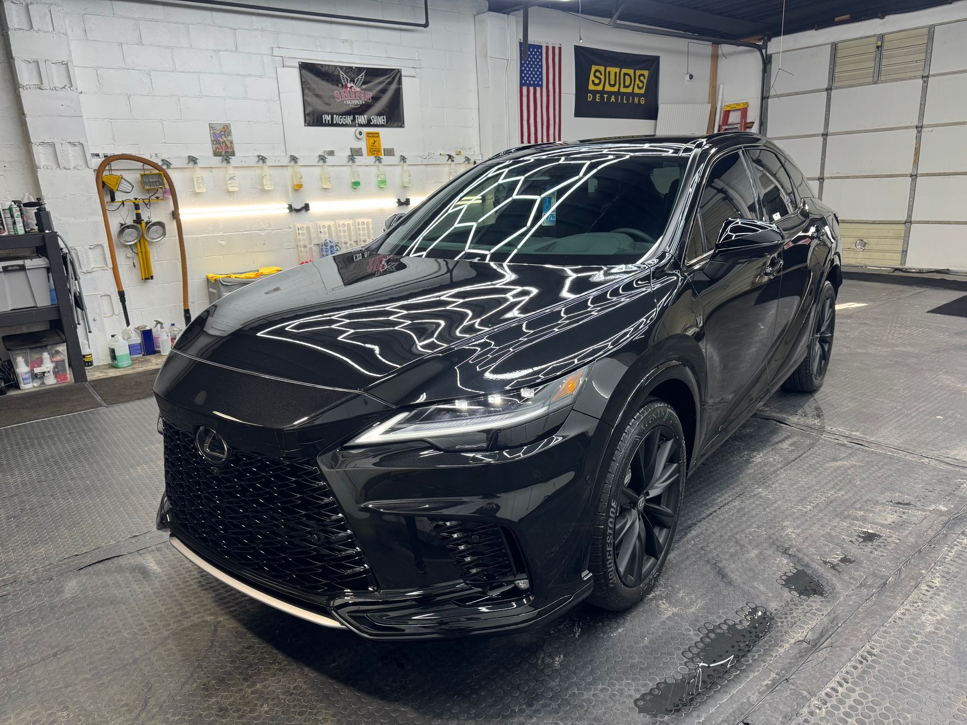 Black SUV in an auto detailing bay with bright overhead reflections on the hood and windshield
