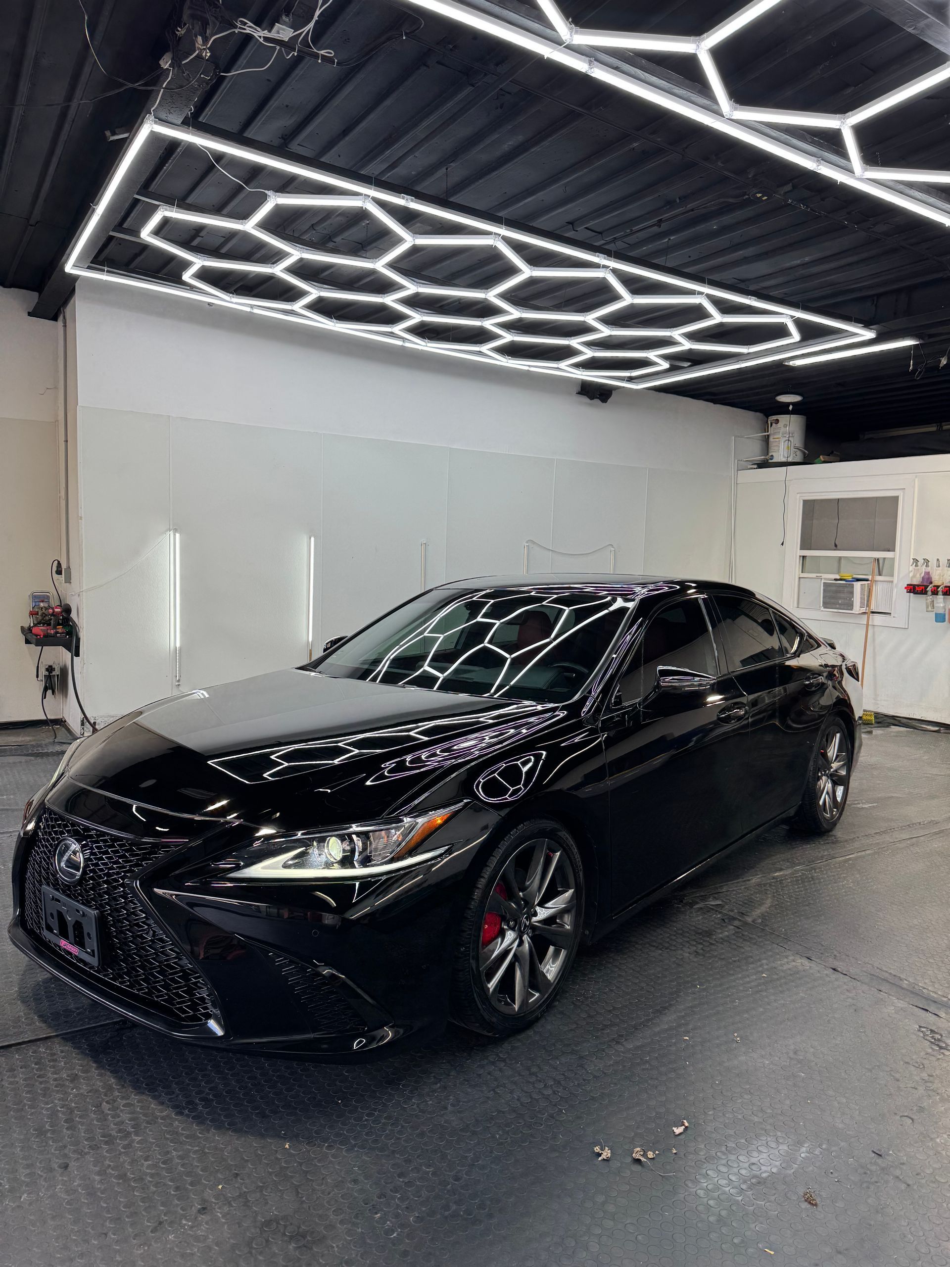 Black sedan in a modern car showroom with geometric ceiling lights.
