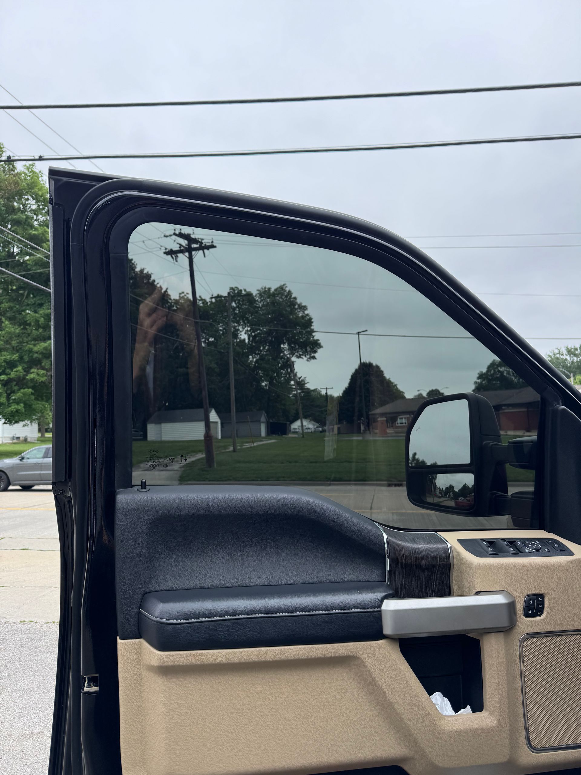 Open car door with black and beige interior, side mirror, and parking lot visible outside.