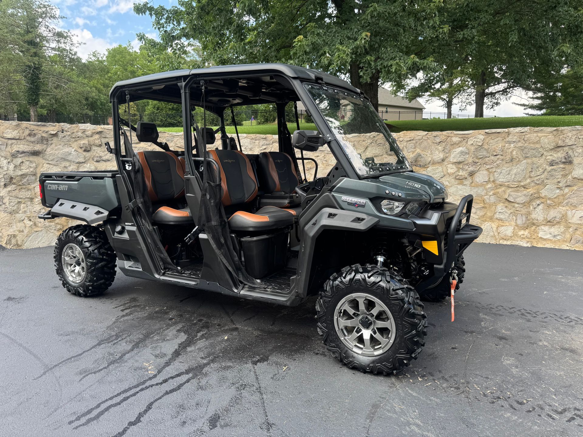 Black off-road UTV with open sides and orange seats parked on wet pavement near a stone wall.