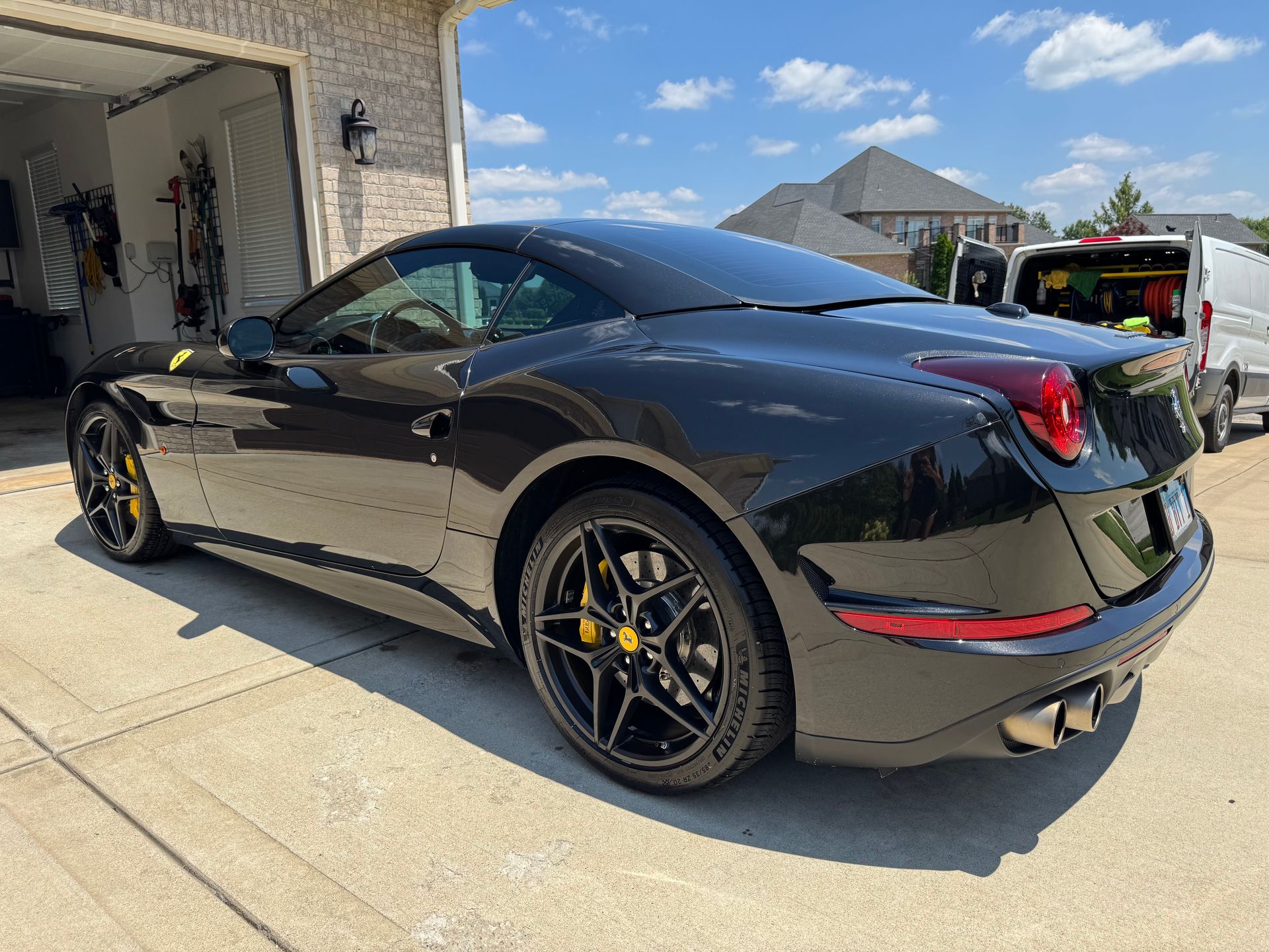 Black sports car parked in a driveway beside a garage, viewed from the rear side.