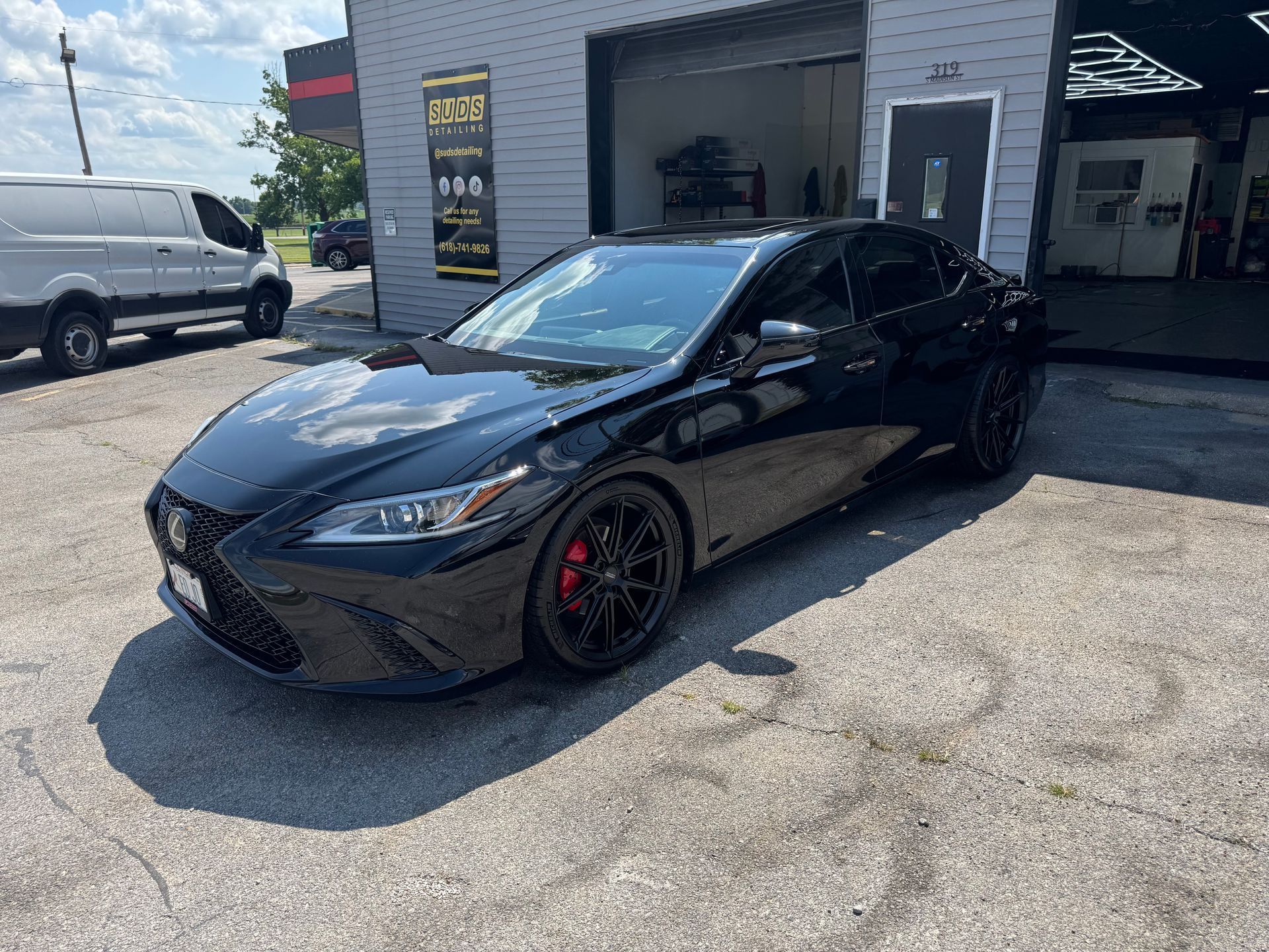 Black sedan parked outside an auto shop in sunlight