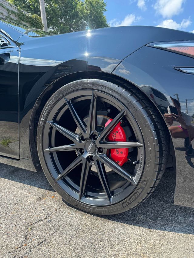 Black sports car close-up with glossy body, black alloy wheel, and red brake caliper.