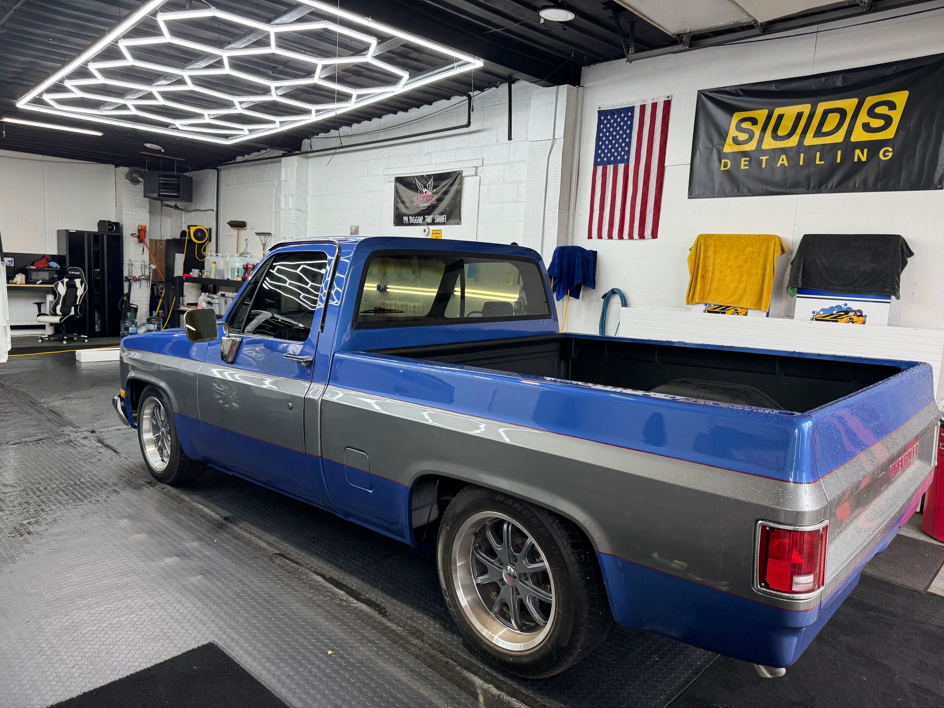 Blue pickup truck inside a car detailing shop with LED ceiling lights and shop banners