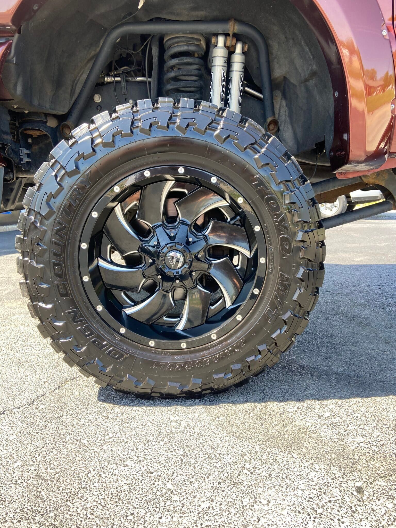 Close-up of a lifted truck’s black off-road tire and wheel with chrome suspension visible above.