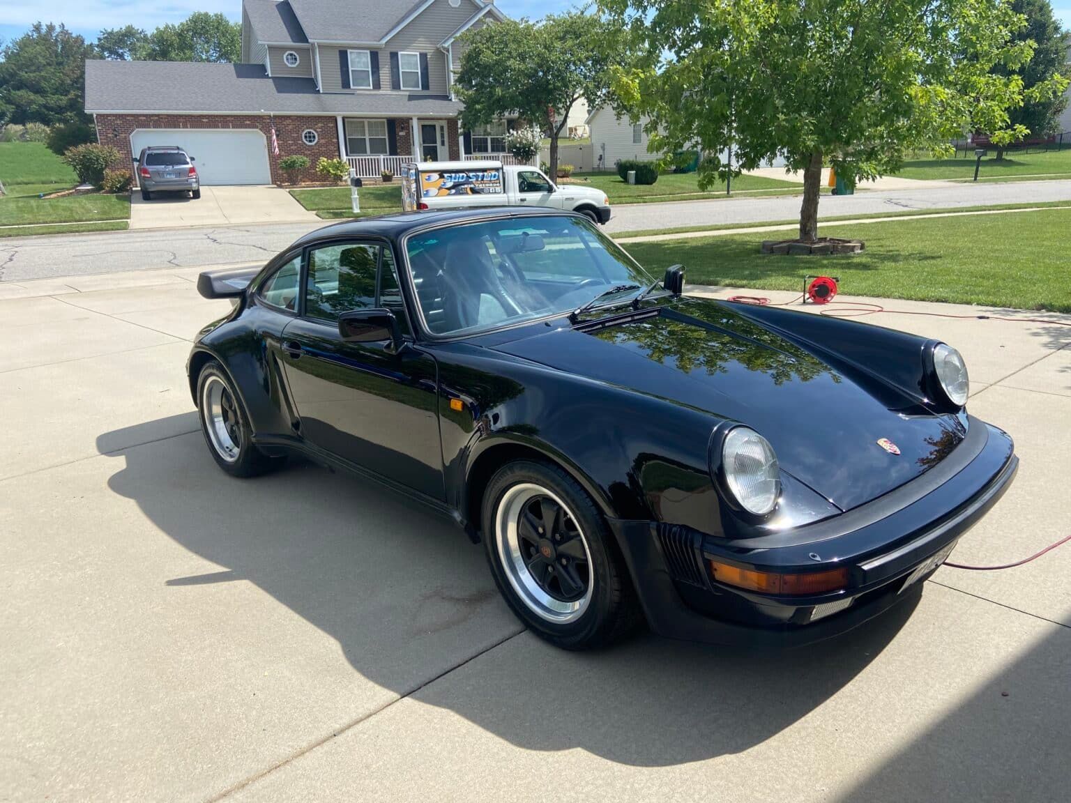 Black classic Porsche 911 parked in a suburban driveway on a sunny day