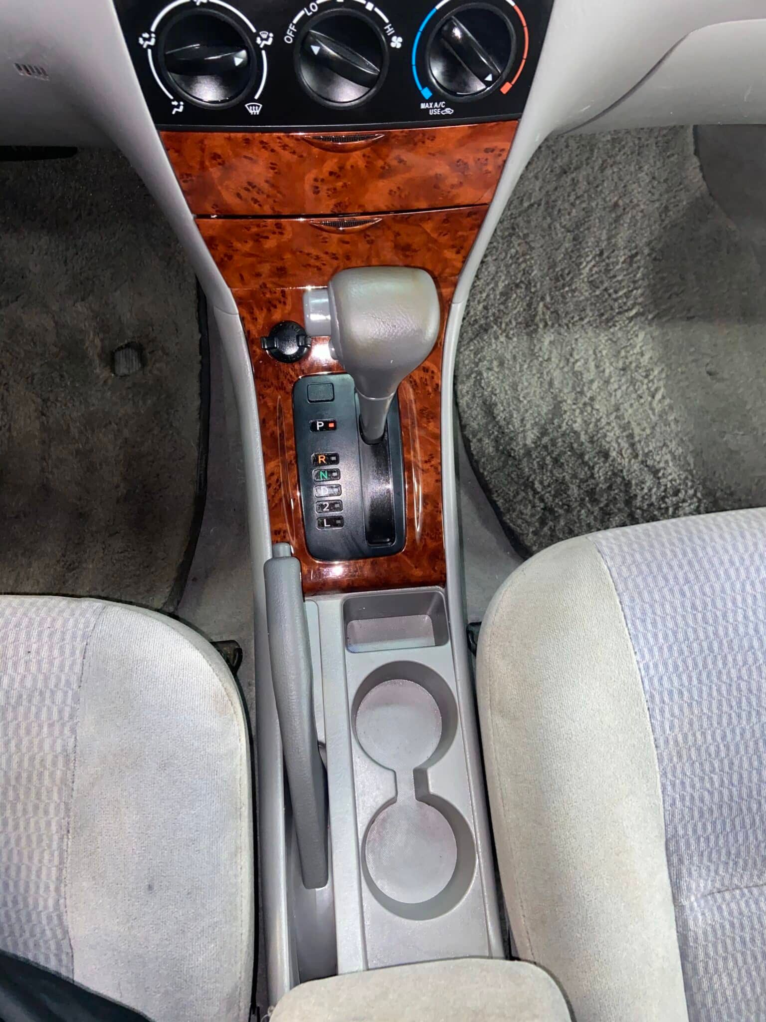 Car interior center console with wood trim, gear shift, cupholders, and climate controls between front seats